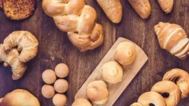 Assortment of fresh baked bread, buns, and pastries on a wooden table.