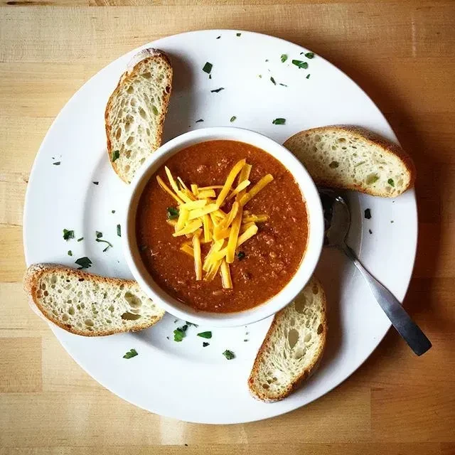 A bowl of chili with shredded cheese and four bread slices.