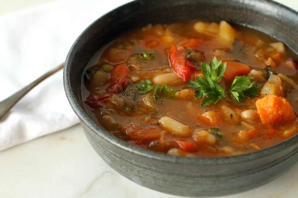 A black bowl of vegetable soup with parsley, a spoon, and napkin.