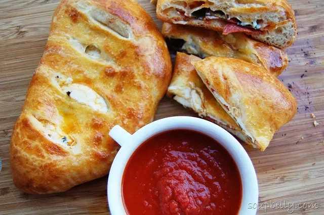 A plate of golden-brown calzones and a small cup of marinara sauce.
