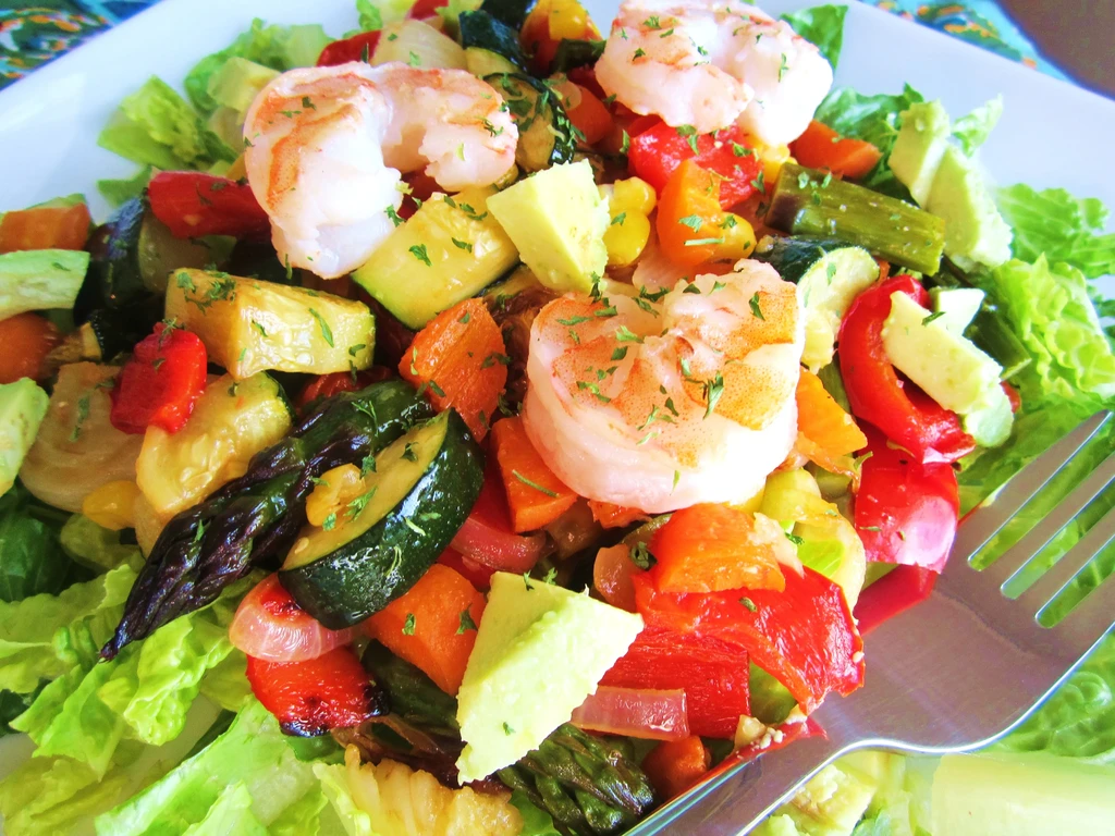 A shrimp salad with roasted vegetables, avocado, and lettuce.