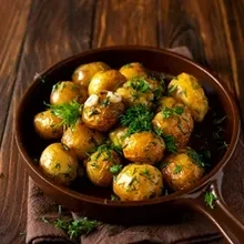 Small roasted potatoes with herbs and garlic in a brown skillet.