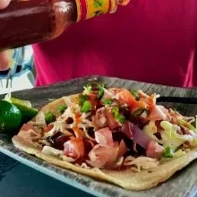 Someone squeezing hot sauce onto a taco topped with ceviche and cabbage.