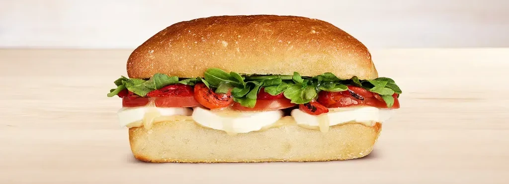 A close-up of a sandwich with mozzarella, tomato, and arugula on a bun.