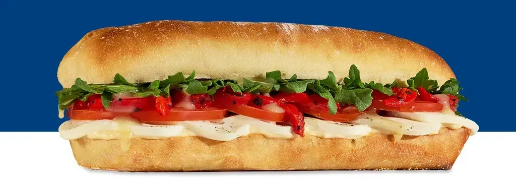A sub sandwich with cheese, tomatoes, roasted red peppers, and arugula.