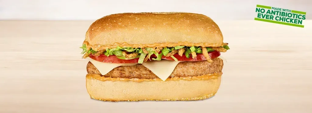 A chicken sandwich on a bun with cheese, lettuce, and tomatoes.