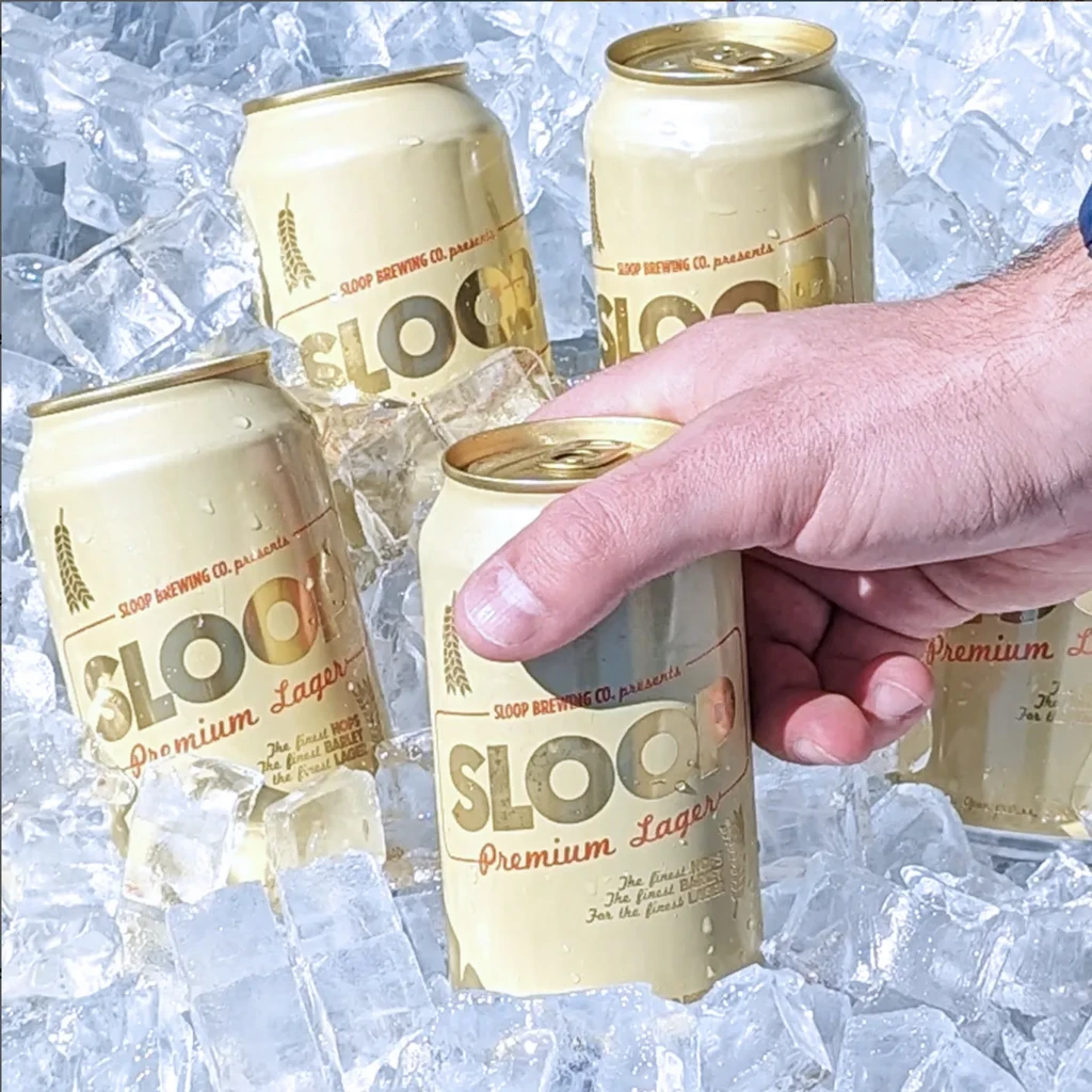 A hand reaches for a can of Sloop Premium Lager in ice.