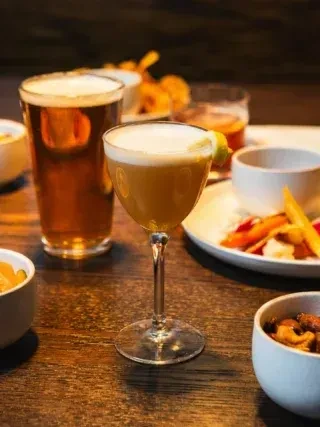 Cocktail, beer, and appetizers on dark wooden table.