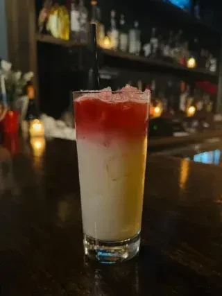 Layered red and pale yellow cocktail with crushed ice and straw.