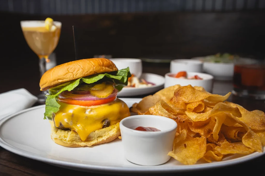 Cheeseburger, crispy potato chips, and ketchup on a white plate.