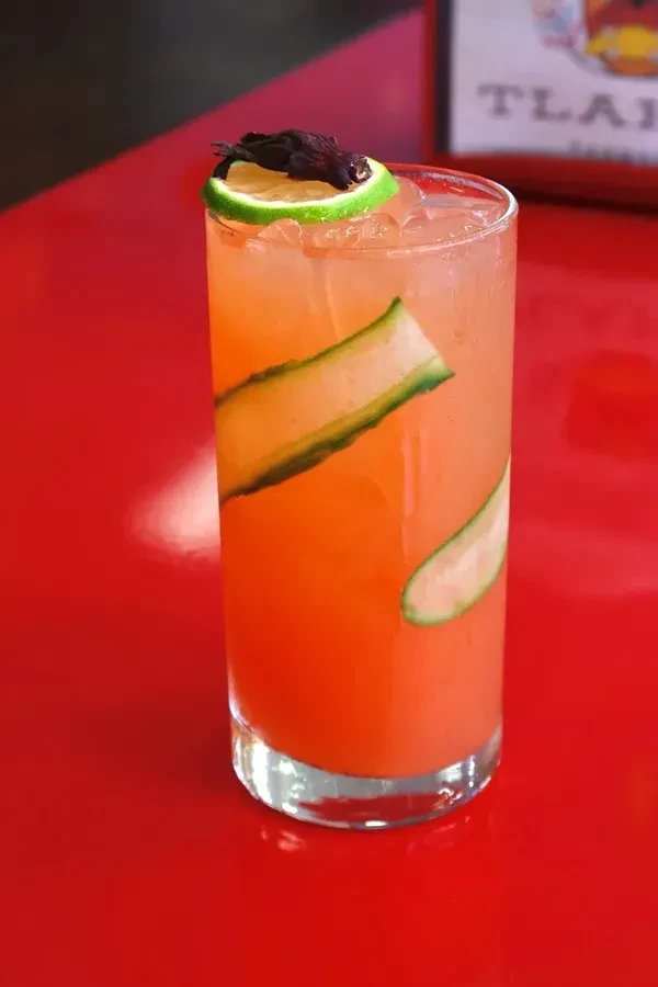 An orange cocktail with cucumber and lime on a red table.