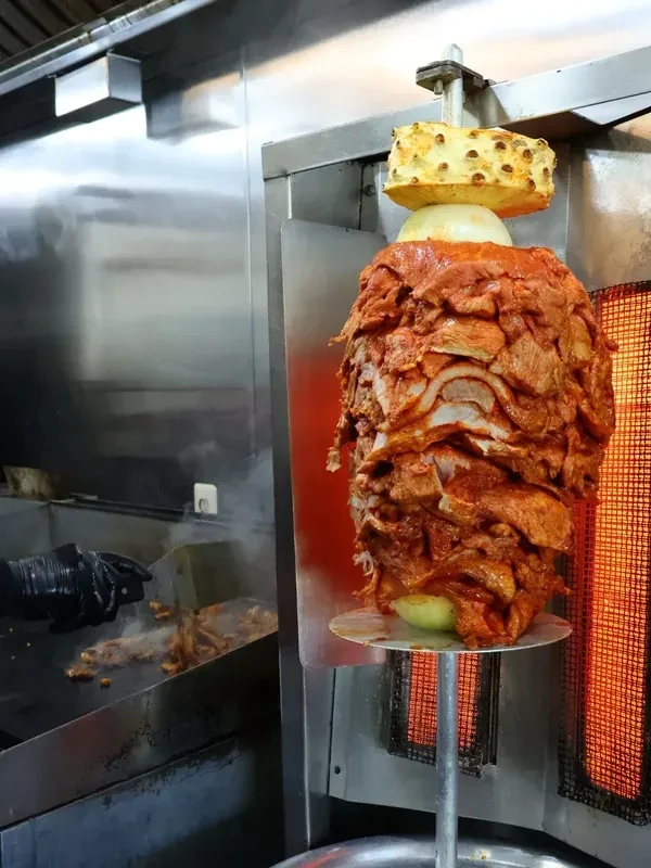 Vertical rotisserie of marinated pork al pastor, topped with pineapple.