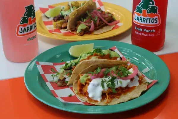 Tacos and Jarritos sodas on plates at a restaurant.