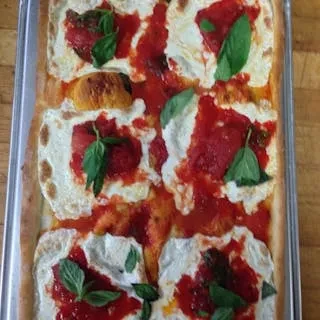 Rectangular pizza with cheese, tomato, and basil in a tray on wood.
