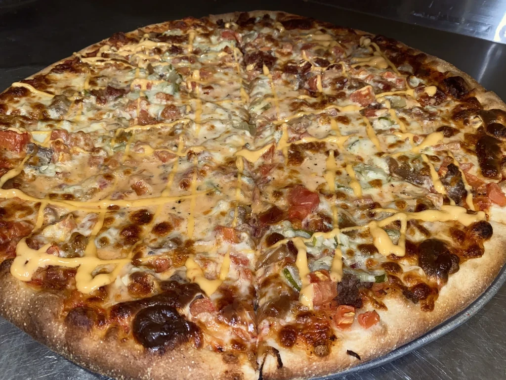 Round pizza with meat, cheese, tomatoes, greens, and orange sauce drizzle.