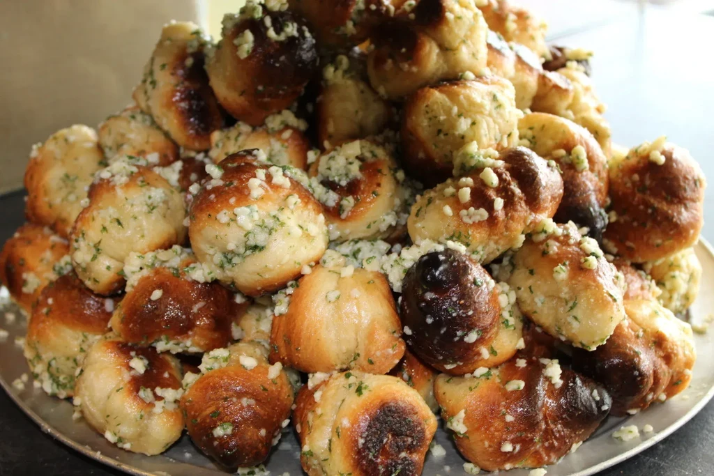 Abundant platter of golden-brown garlic knots topped with garlic and herbs.