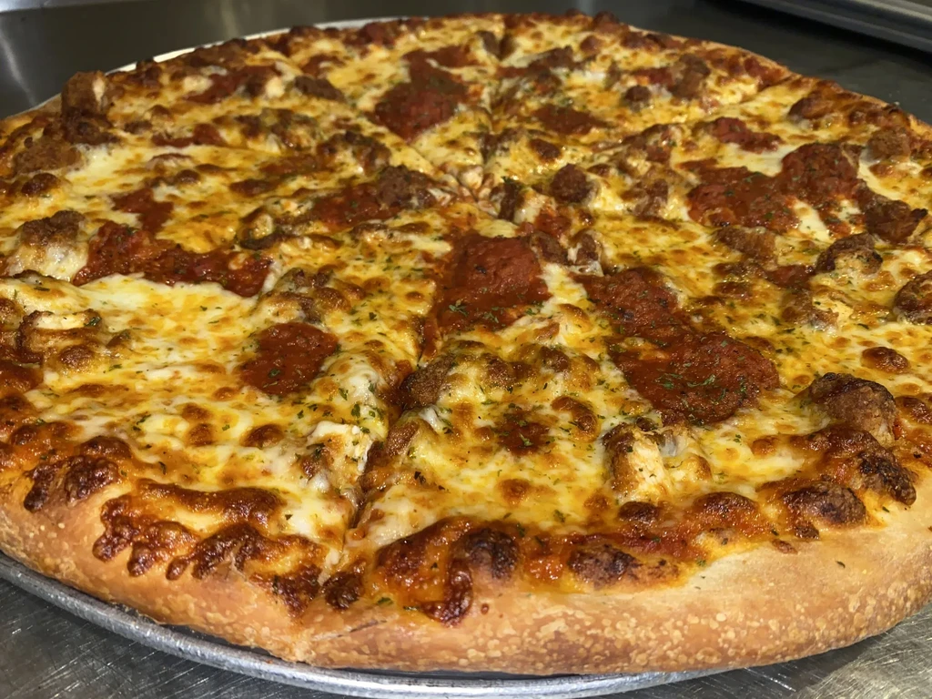 Cooked round pizza with meat, melted cheese, and herbs on a pan.