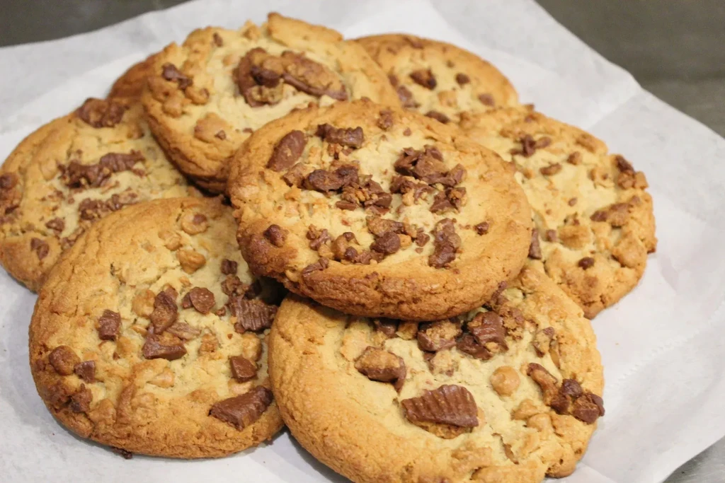 Pile of golden-brown cookies studded with chopped peanut butter cups.