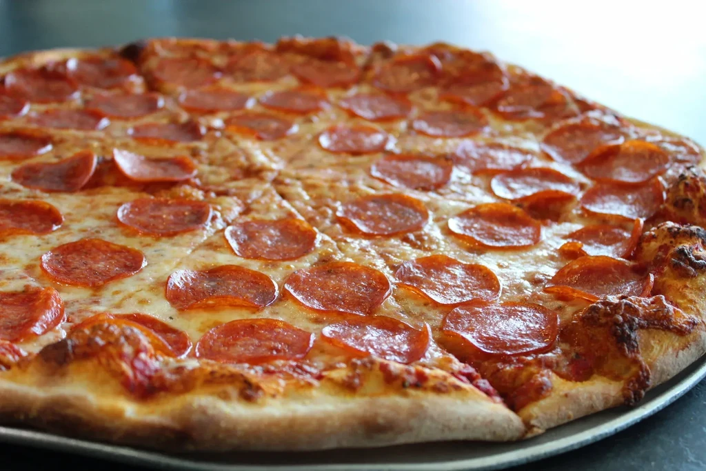 Round pepperoni pizza with melted cheese, golden crust, on a metal pan.