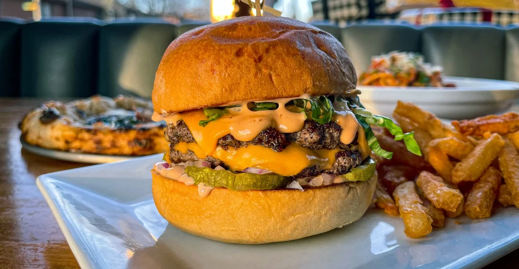 Close-up of a double cheeseburger with fries, pizza, and pasta.