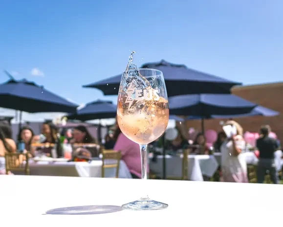 A wine glass with splashing liquid, outdoors at a sunny event.