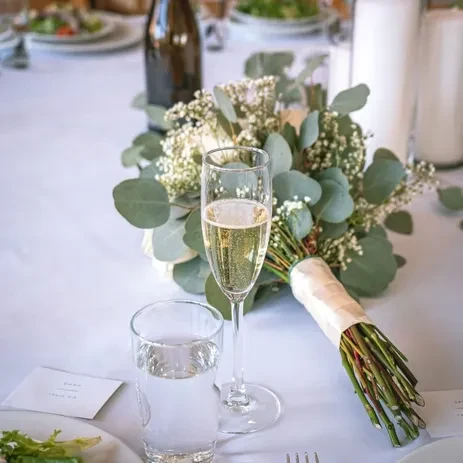 A champagne flute next to a wedding bouquet on a white table.