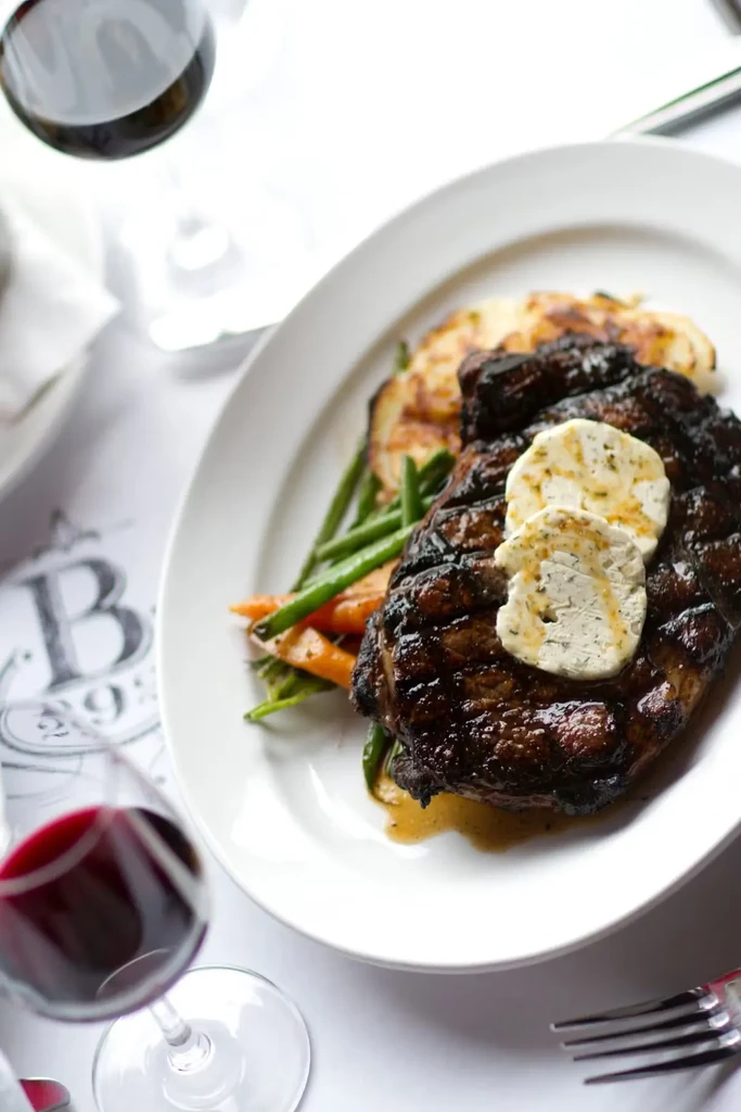 Grilled steak with herb butter, vegetables, and potatoes, with red wine.