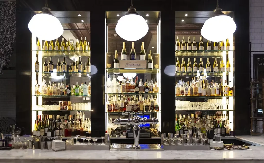 A brightly lit bar with three large shelves of wine and liquor bottles.