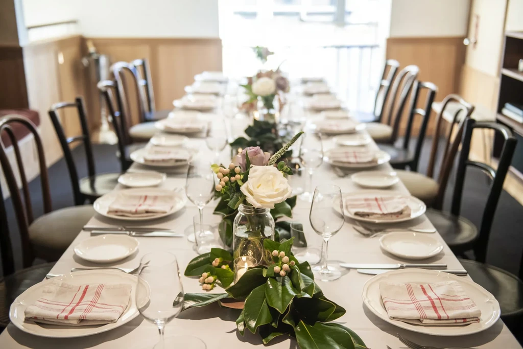 Long dining table set with white place settings, flowers, and lit candles.
