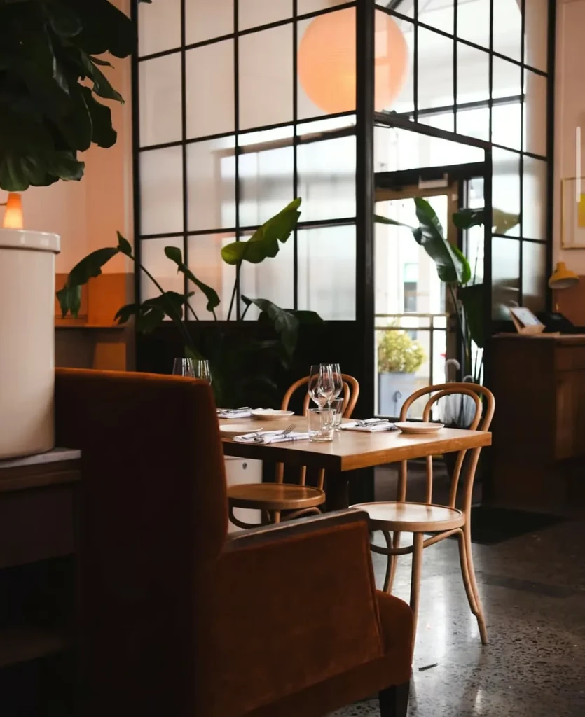 Modern restaurant interior with a set dining table, armchair, and green plants.