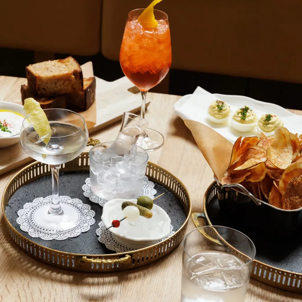 Cocktails, deviled eggs, chips, and olives on a wooden table.