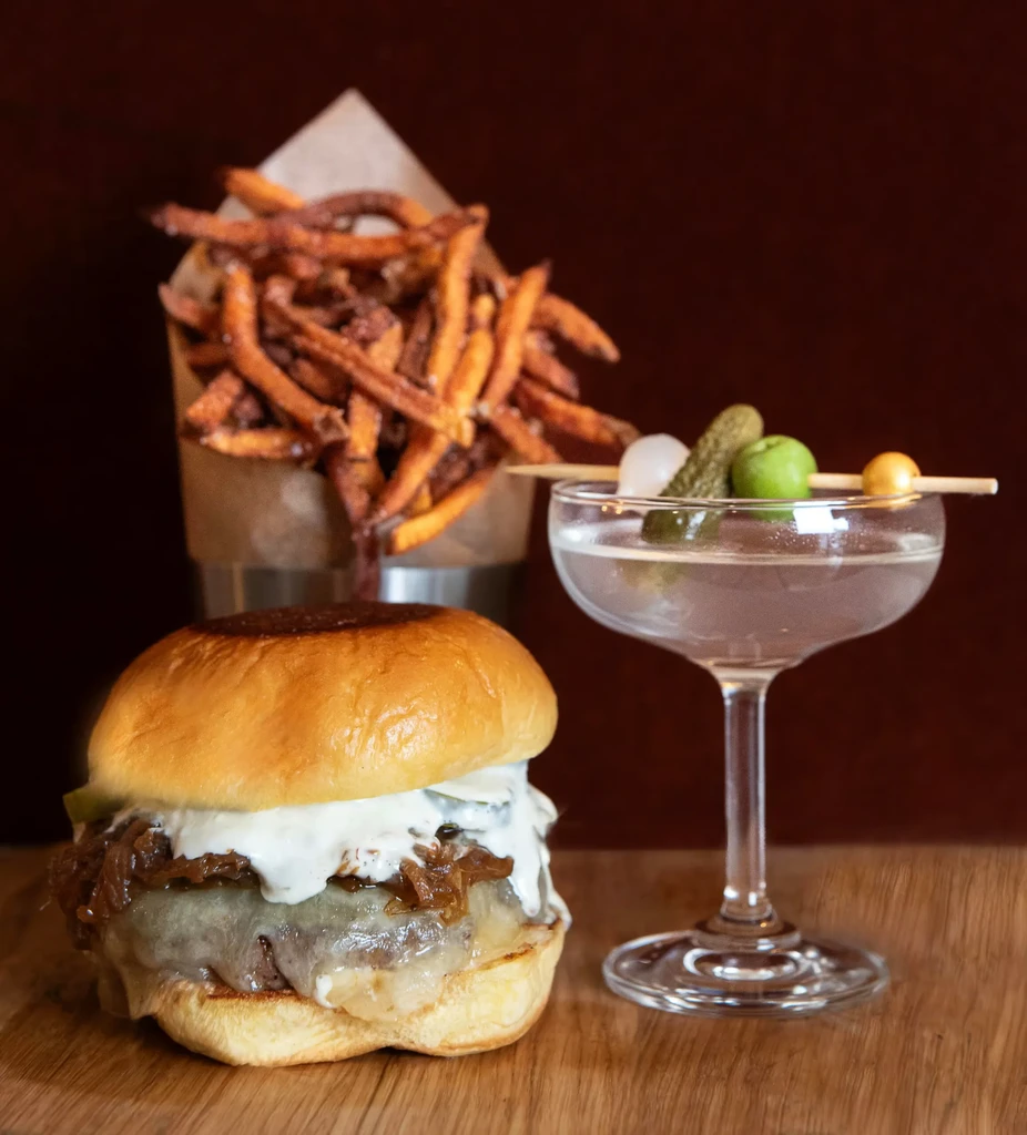 A gourmet burger, sweet potato fries, and a garnished cocktail.