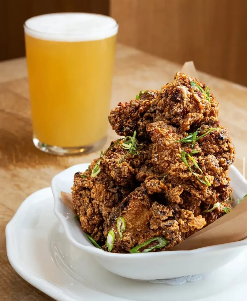 A bowl of crispy fried chicken and a glass of foamy amber beer.