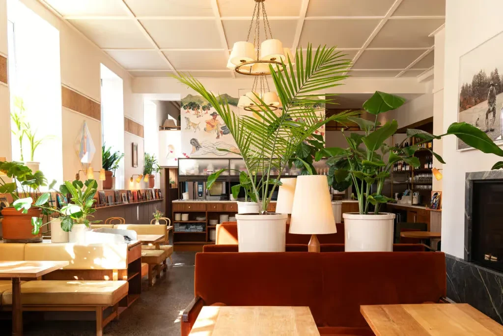 Spacious, modern restaurant with abundant green plants, diverse seating, and a mural.