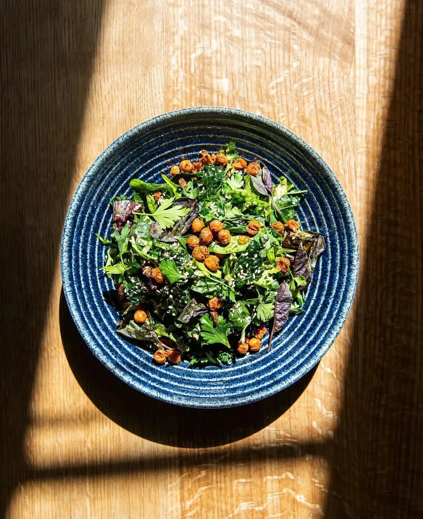 Green salad with roasted chickpeas and sesame in a blue bowl.