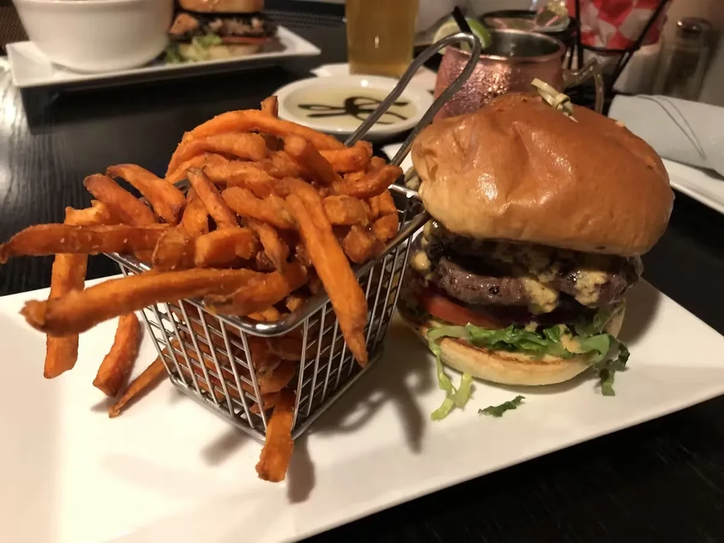 A double cheeseburger with sweet potato fries on a white plate.