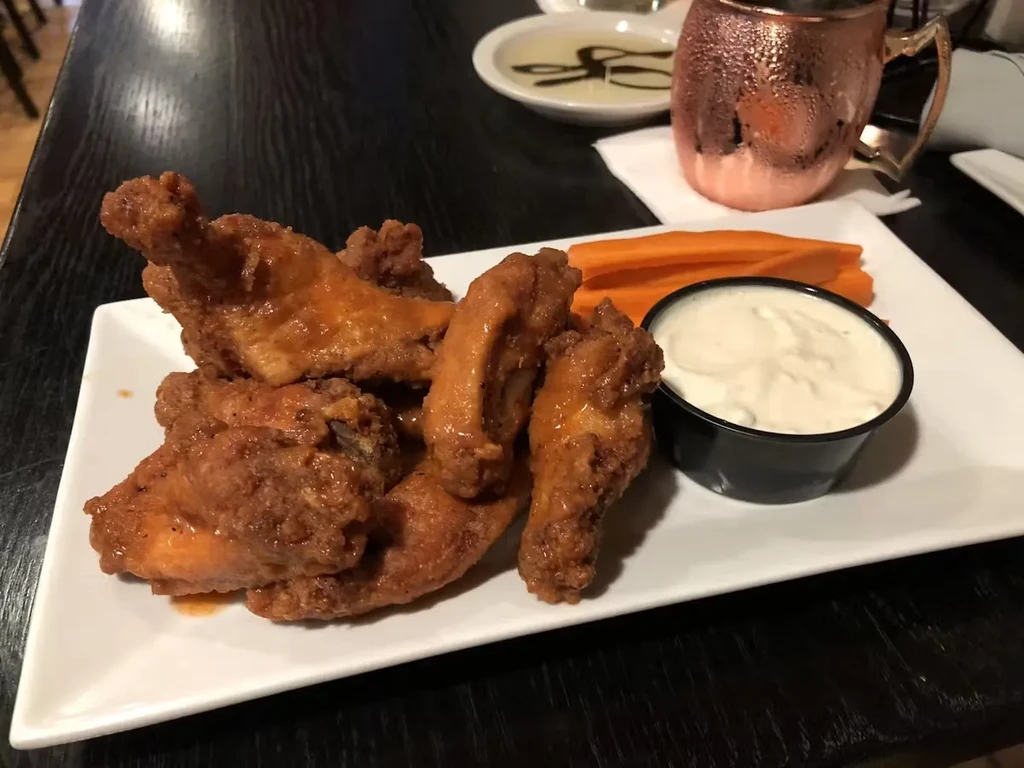 Chicken wings with dipping sauce and carrot sticks on a white plate.