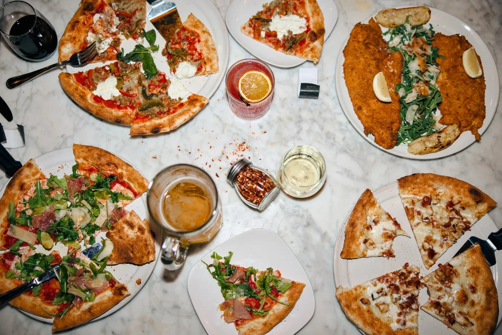 Overhead view of a marble table covered with pizza, food, and drinks.