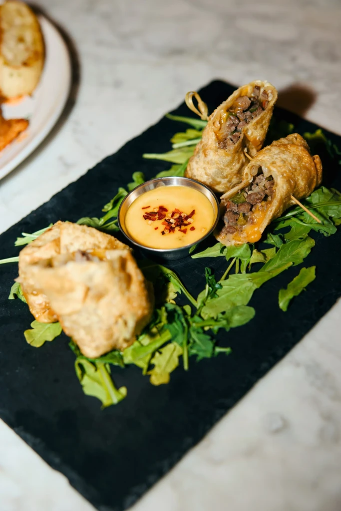 Three crispy egg rolls with meat and cheese, with a dipping sauce.