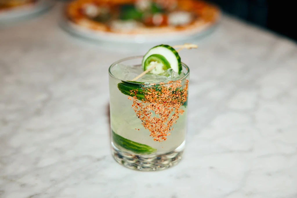 A cucumber cocktail with red chili flakes on a marble table.