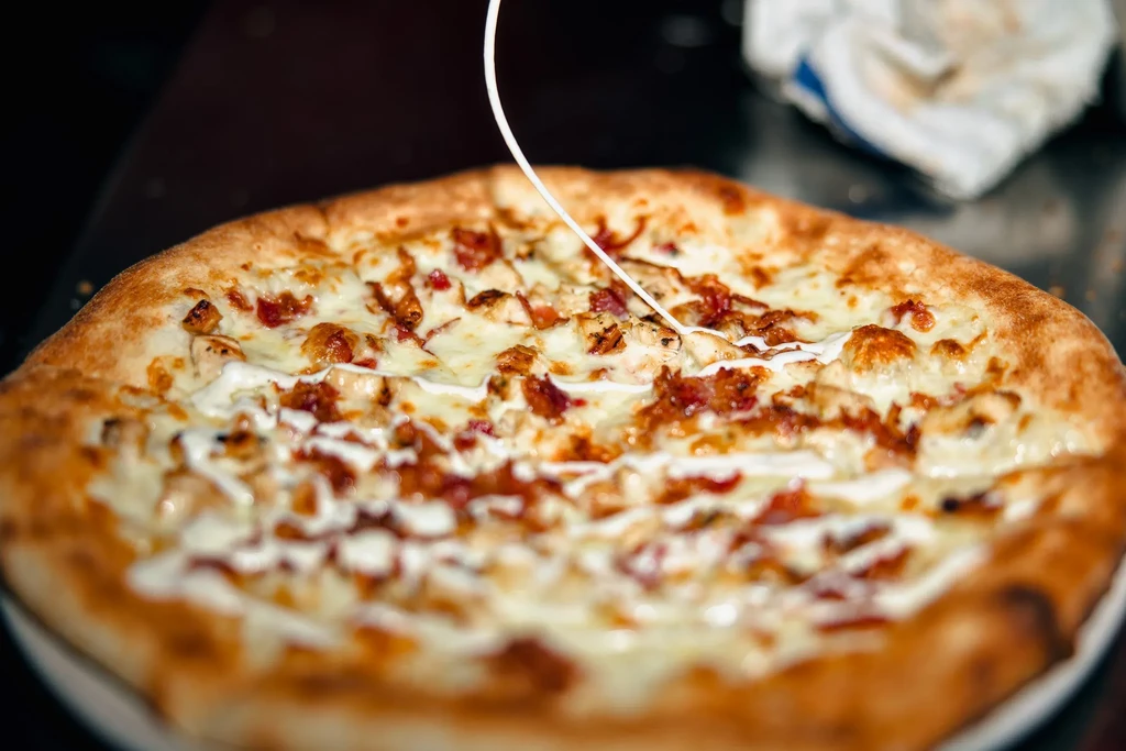 Close-up of a white sauce pizza with chicken and bacon.