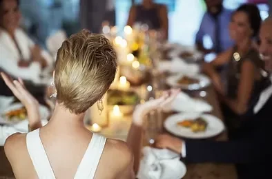 Woman from behind at candlelit table with blurred guests.