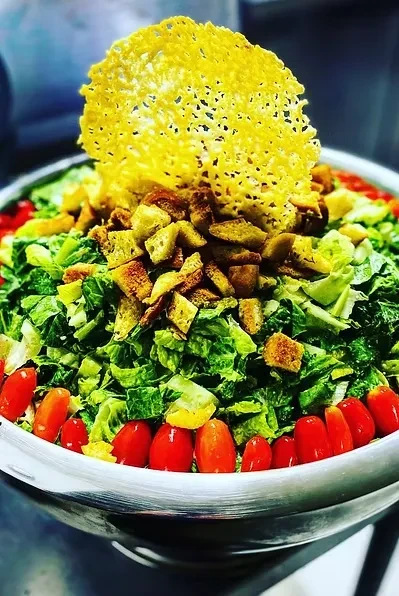 Caesar salad with parmesan crisp, croutons, and tomatoes in metal bowl.