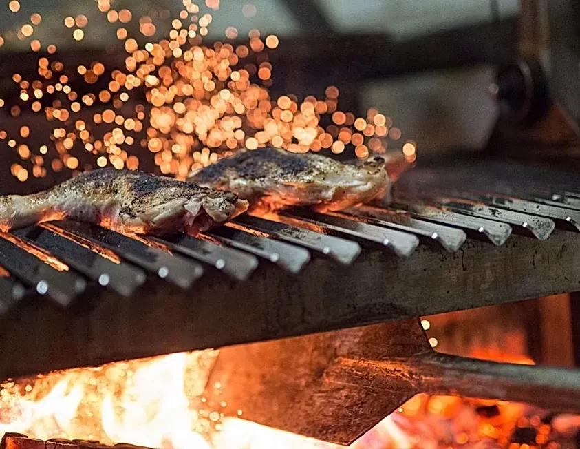Seasoned chicken grilling over open flames, sparks rising into dark.