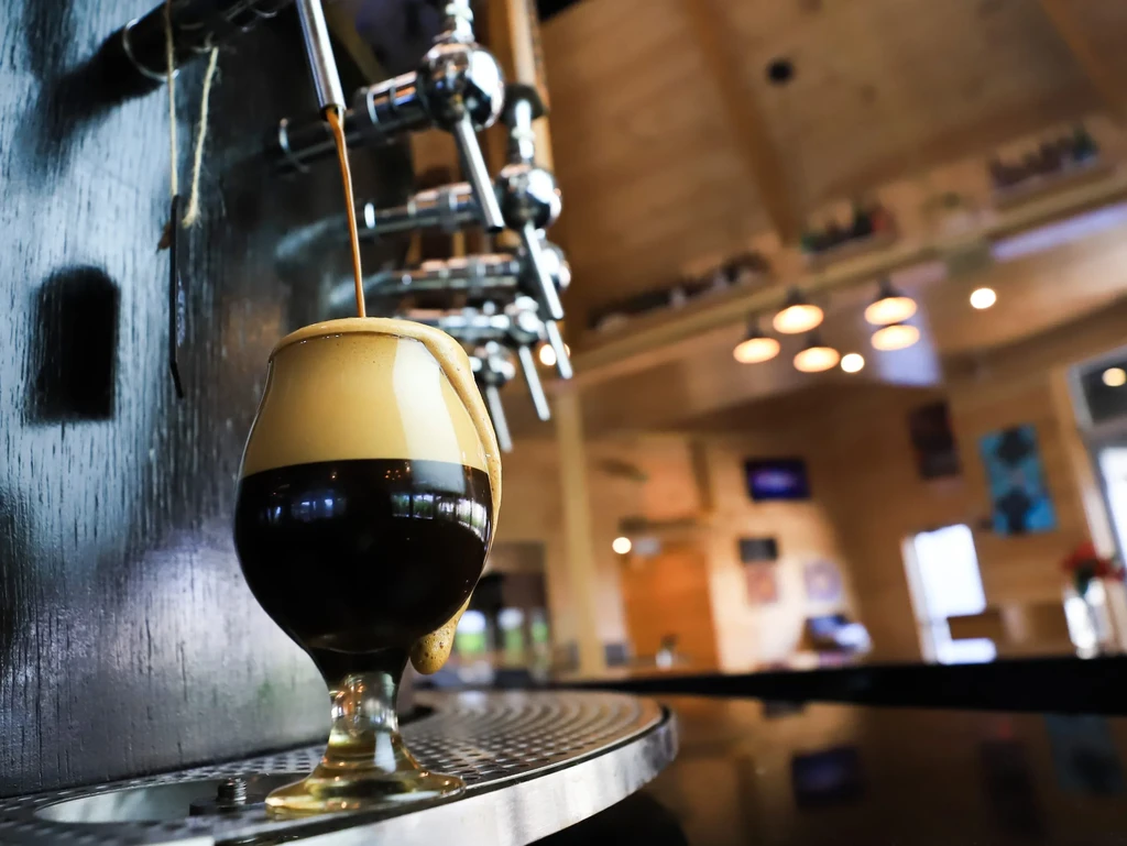 Dark beer poured into a stemmed glass with overflowing creamy head.