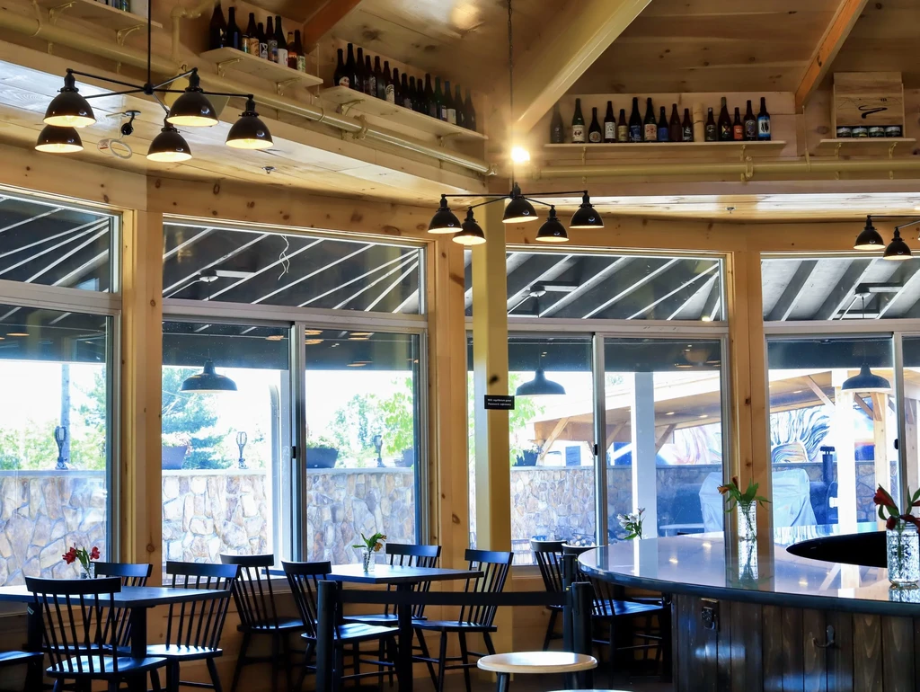 Modern rustic restaurant interior with wooden beams, a bar, and patio view.