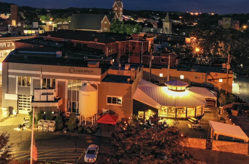 Aerial night view of Equilibrium brewery complex with lit patio.