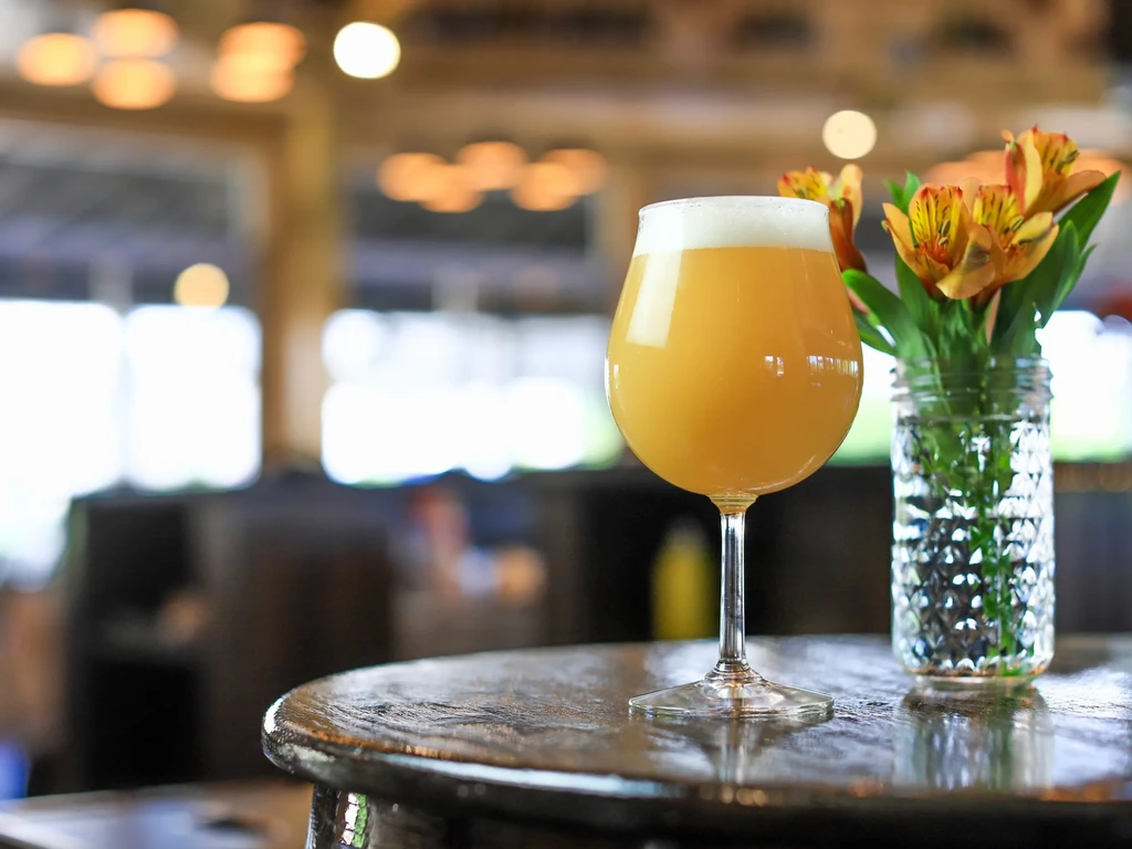 Hazy golden beer and orange flowers on a rustic wooden table.