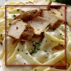 Fettuccine Alfredo pasta topped with seasoned sliced chicken and parsley.