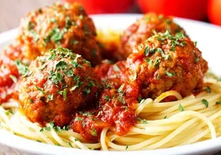 Spaghetti with five large meatballs, covered in red sauce and parsley.
